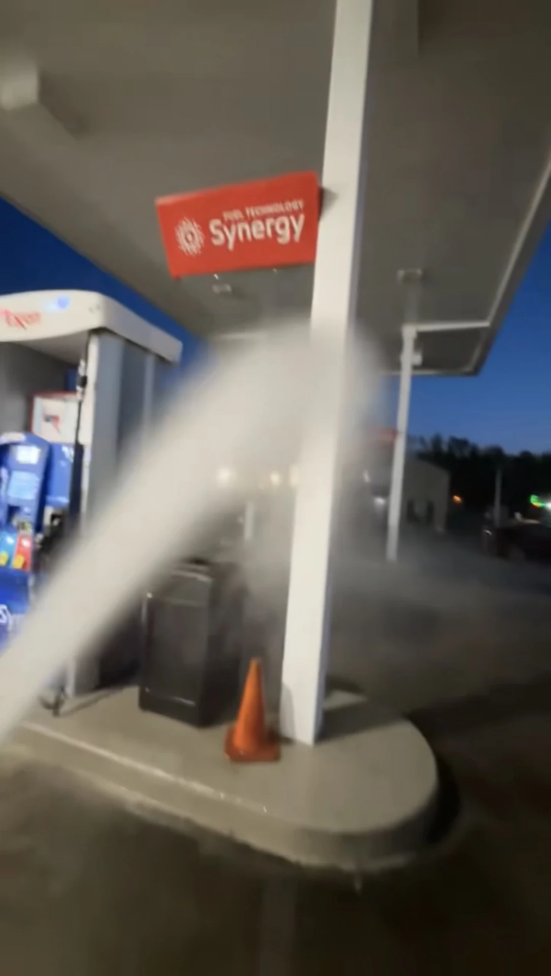 Pressure washing the concrete under a gas station canopy at dusk